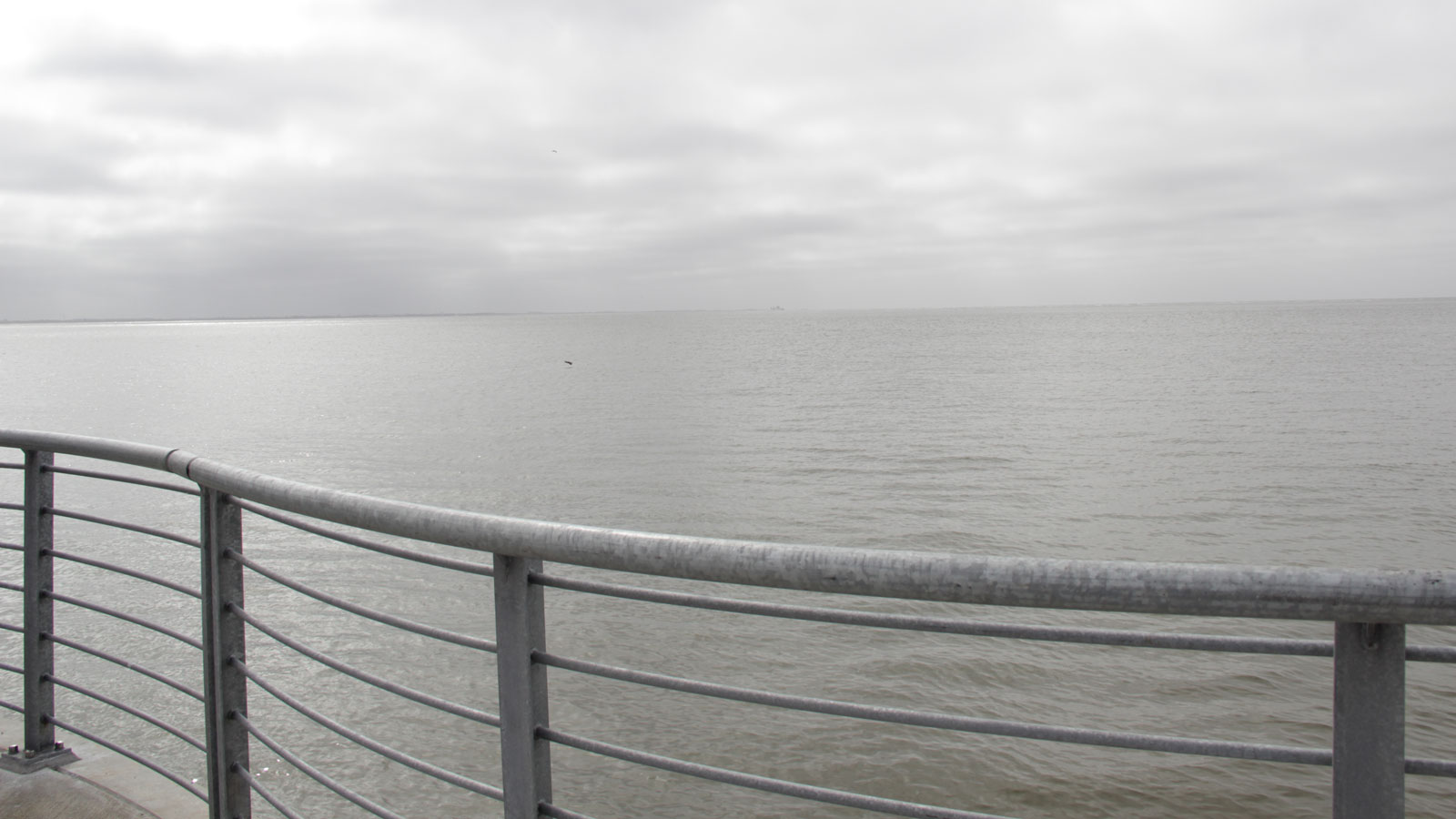 ein geschwungenes Metallgeländer, dahinter der Blick auf die See und den Himmel