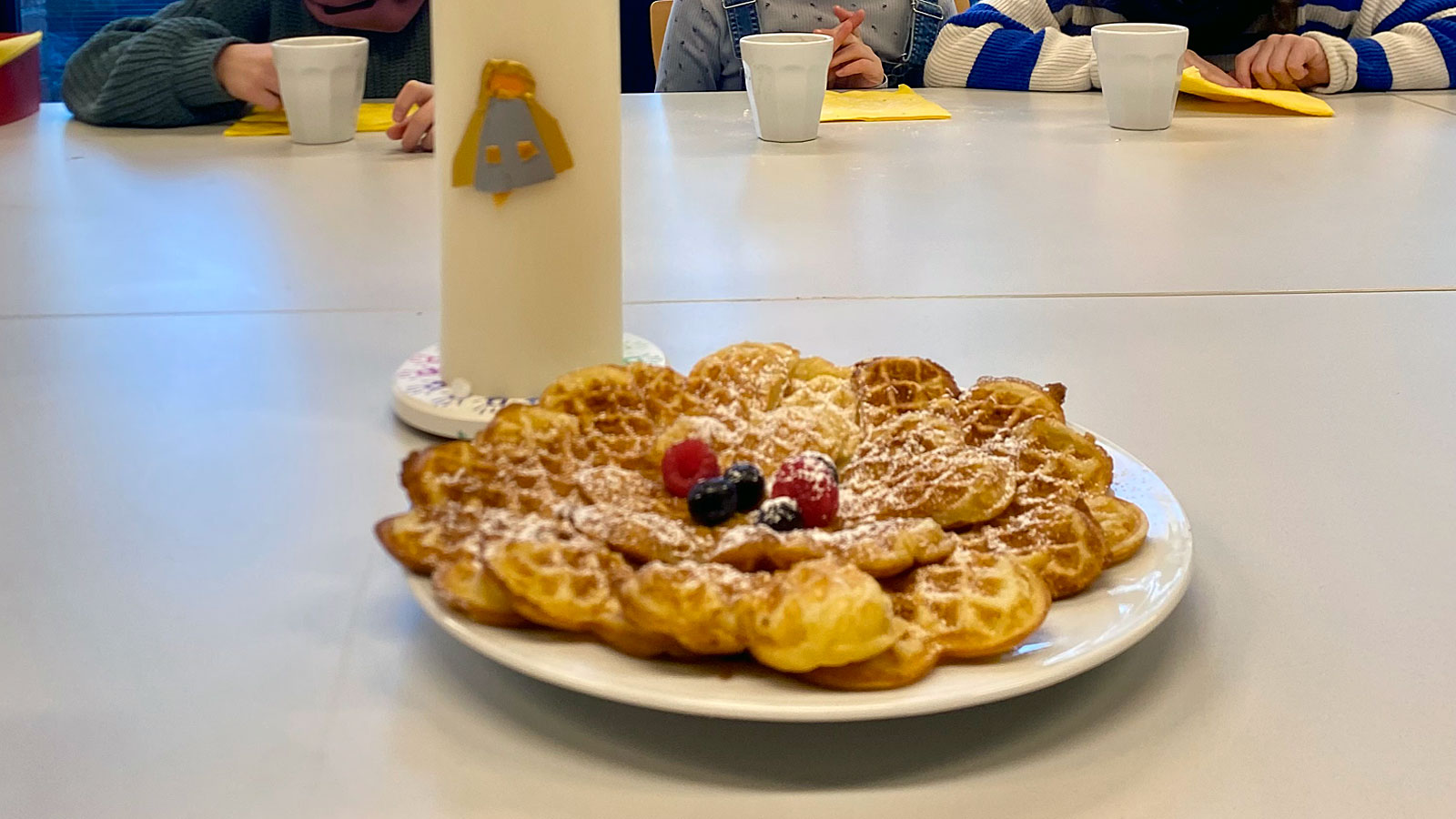 weißer Tisch, darauf eine Kerze mit Engelmotiv, im Vordergrund ein Teller mit selbstgebackenen Waffeln