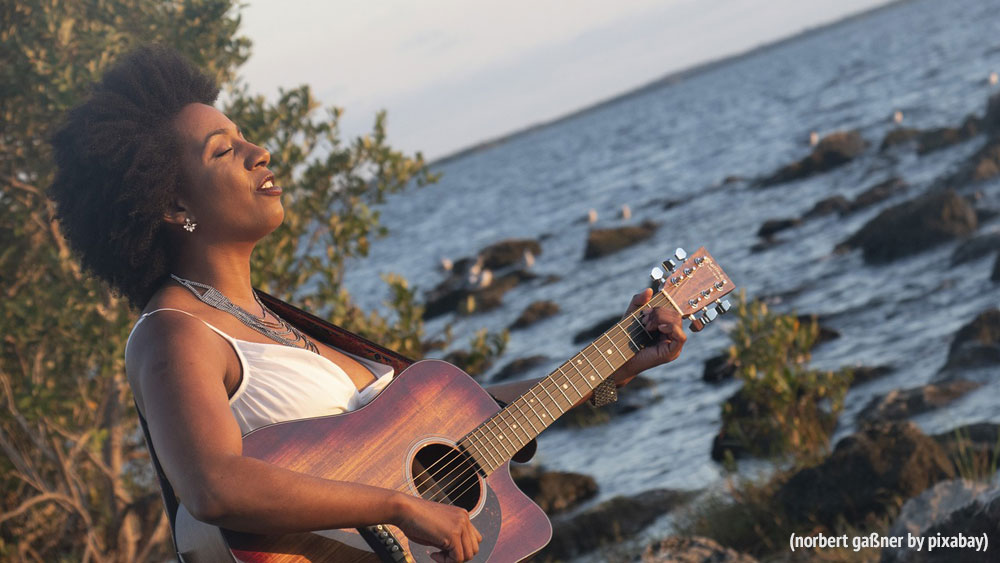 Symbolbild: Frau mit Gitarre am Meer